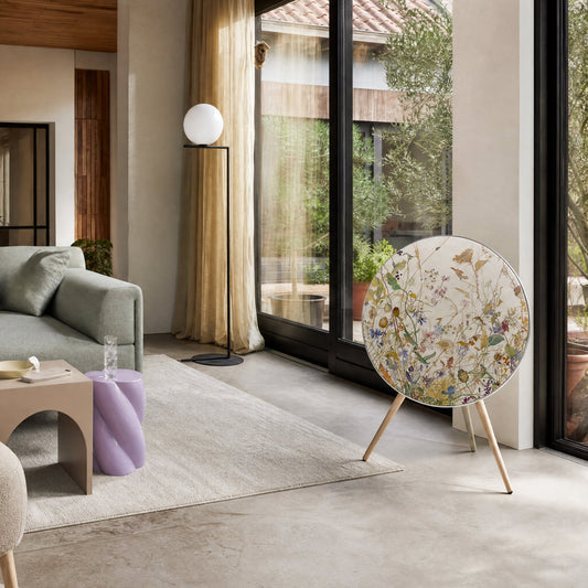 Bang & Olufsen BeoPlay A9 with the Herbarium cover by Tegrino Studio in a sunlit living room beside a green sofa