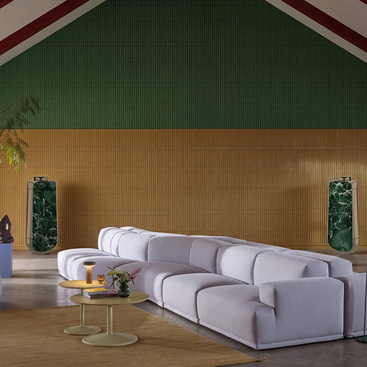 Bang & Olufsen BeoLab 50 in Verde St. Denis green marble skins, styling a living room with a grey modular sofa and wood-panelled wall
