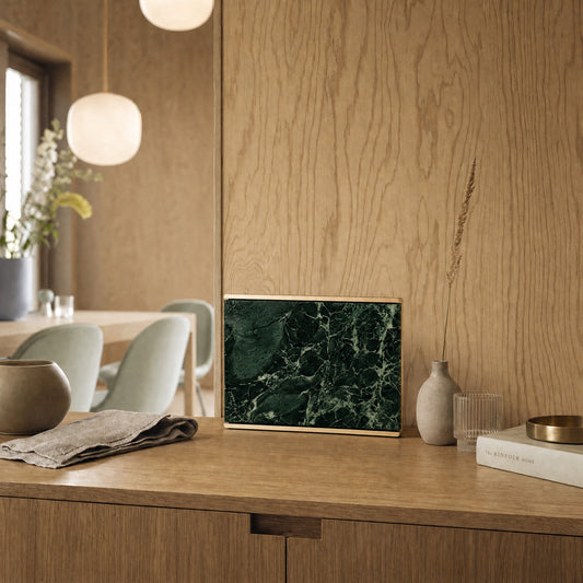 Bang & Olufsen BeoSound Level with Verde St. Denis green marble skin on an oak sideboard beside a dining table with pendant lamps and a ceramic vase