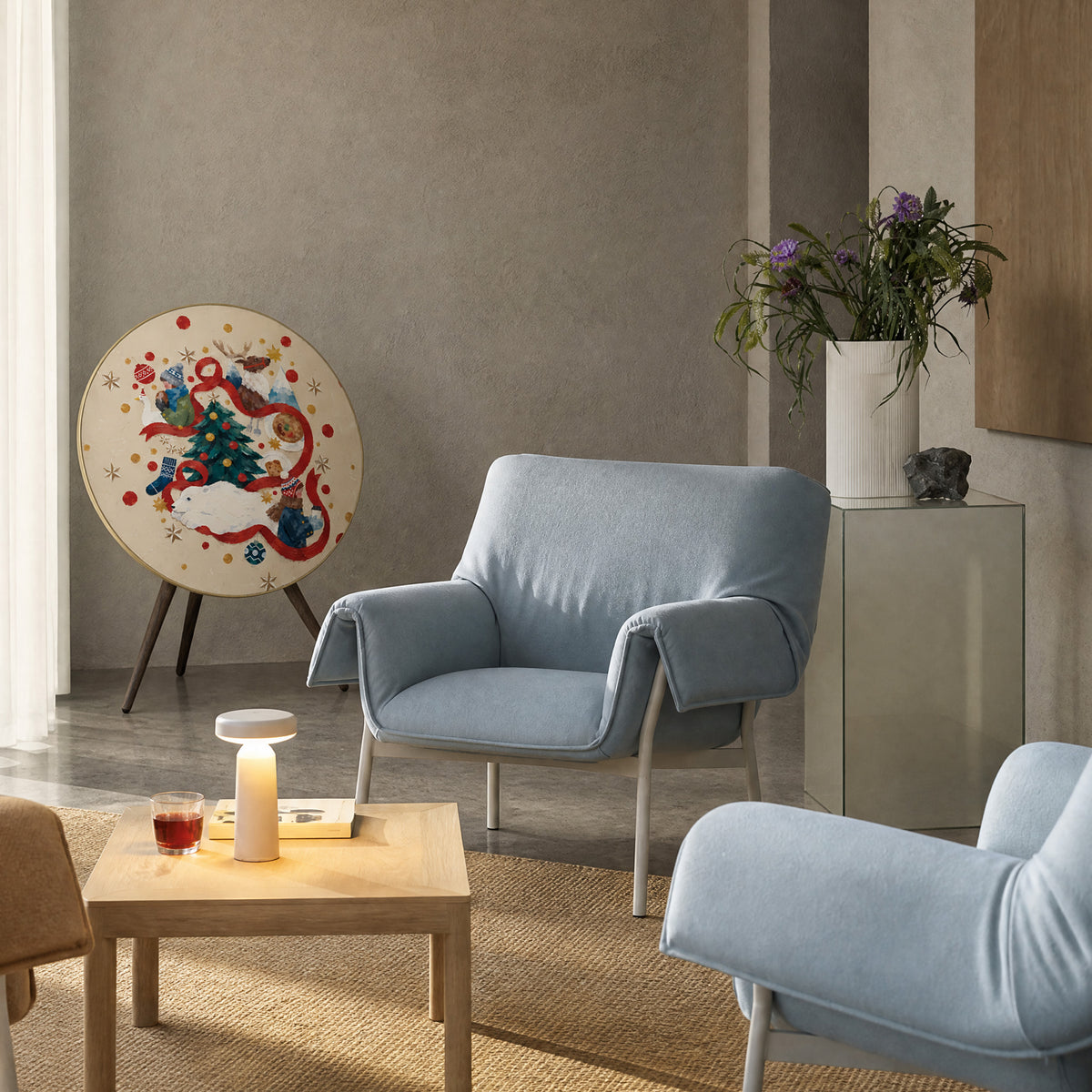 Bang & Olufsen Beosound A9 speaker with the Christmas Tale cover by Tegrino Studio in a calm living room with pale blue armchairs, showing a gouache winter story with a red ribbon and a decorated tree