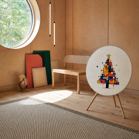 Bang & Olufsen Beosound A9 speaker with the Mondrian Noël cover by Tegrino Studio in a warm wooden room with a round window and coloured panels leaning on the wall, showing a Christmas tree of red, yellow and blue blocks