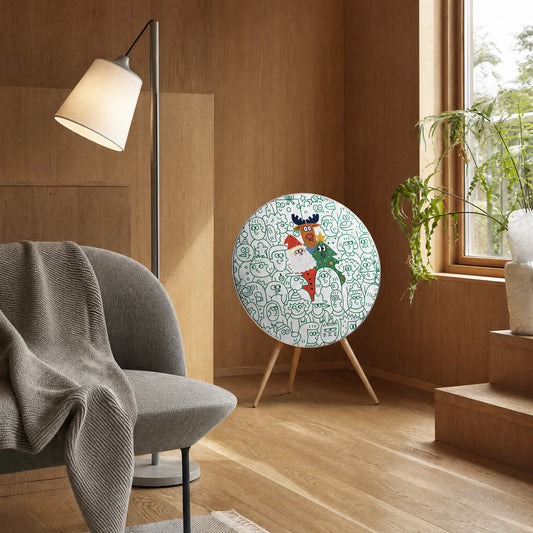 Bang & Olufsen Beosound A9 speaker with the Spot the Santa cover by Tegrino Studio in a warm wood-panelled room beside a floor lamp and a grey armchair, showing Santa, a reindeer and a Christmas tree in a green-line crowd