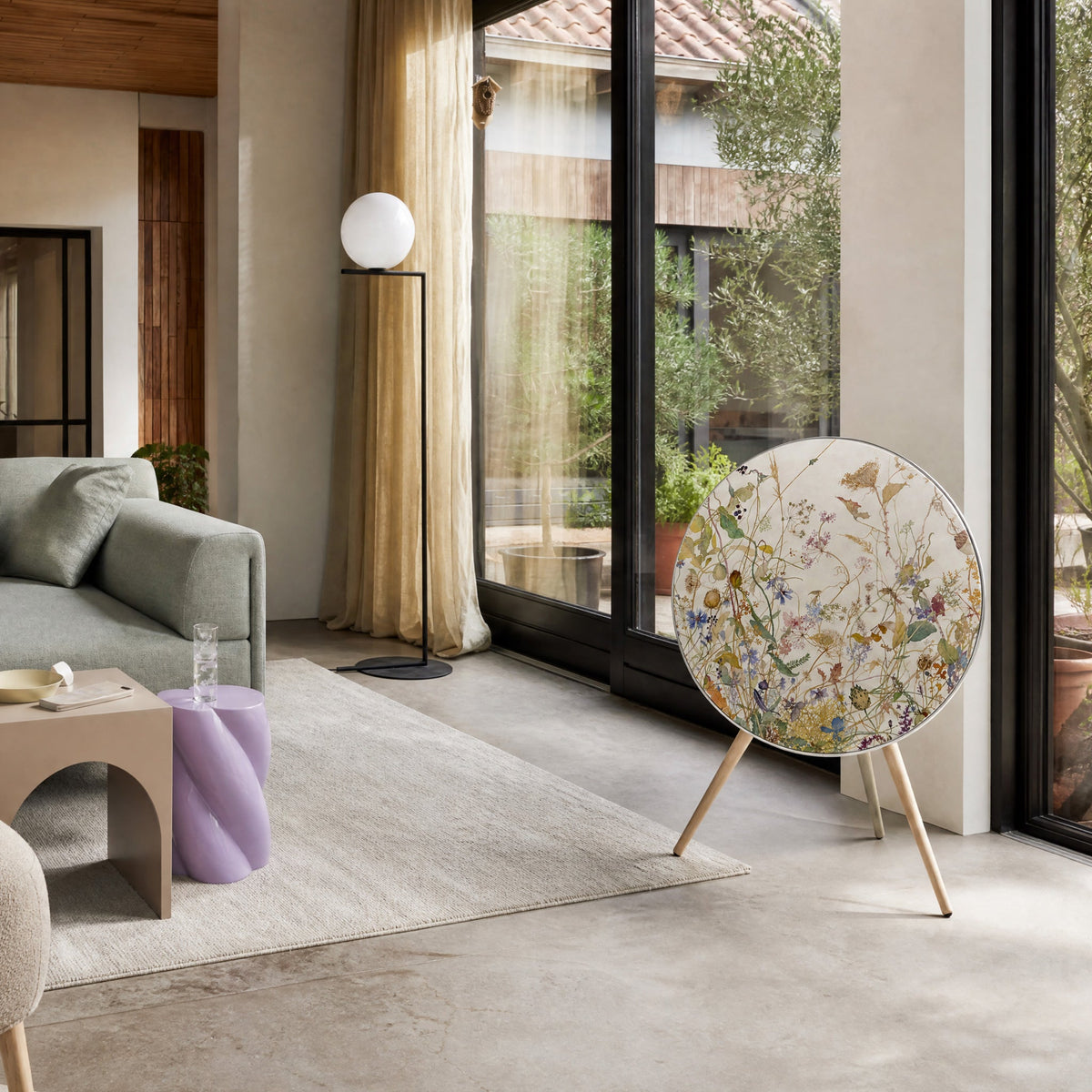 Bang & Olufsen BeoPlay A9 with the Herbarium cover by Tegrino Studio in a sunlit living room beside a green sofa