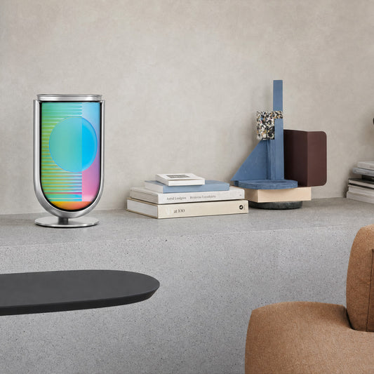 Bang & Olufsen BeoLab 8 speaker cover Prism by Tegrino Studio in a minimalist home environment, featuring full-spectrum gradient with holographic sphere in teal, blue and pink on grey stone shelf beside Scandinavian art books and geometric sculpture with tan armchair