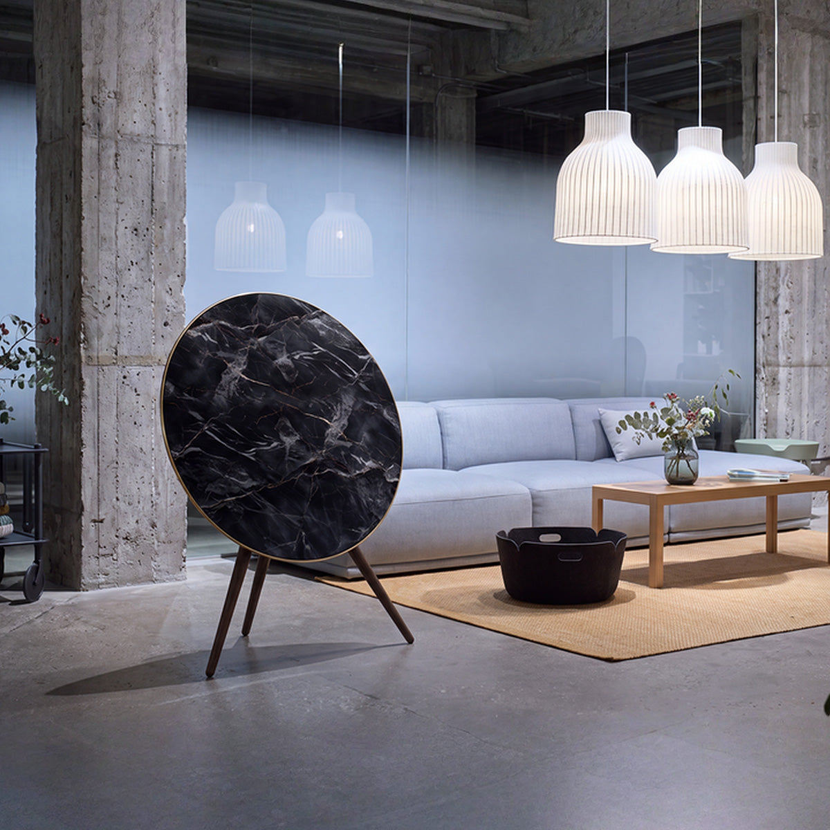 Bang & Olufsen BeoPlay A9 and BeoSound A9 speaker with Noir Marquina black marble skin displayed in industrial-style loft with concrete columns, pendant lighting, and light gray sofa