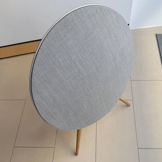 Bang & Olufsen BeoPlay A9 and BeoSound A9 Kvadrat cover Natural by Bang & Olufsen in a minimalist home environment, featuring light natural grey wool blend textile on oak legs beside a Danish toy soldier figurine with natural daylight from window