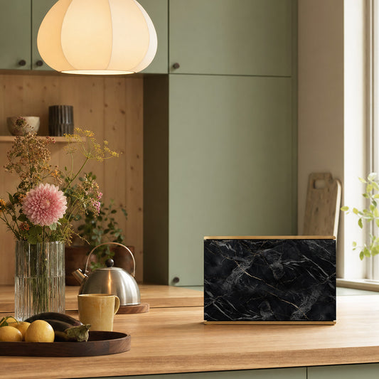 Bang & Olufsen BeoSound Level skin in Noir Marquina black marble design with gold veining displayed on wooden kitchen counter beside fresh flowers and pendant lamp in sage green kitchen