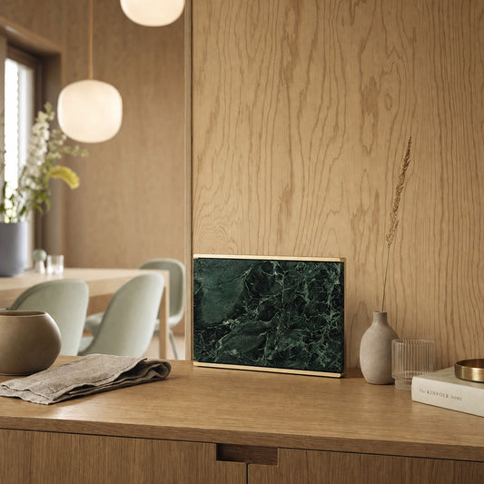 Bang & Olufsen BeoSound Level with Verde St. Denis green marble skin on an oak sideboard beside a dining table with pendant lamps and a ceramic vase