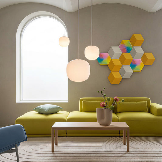 Bang & Olufsen BeoSound Shape speaker cover Prism by Tegrino Studio in a curated home space, highlighting full-spectrum gradient tiles mixed with solid amber yellow and warm grey hexagonal panels on taupe wall above chartreuse sofa with globe pendant lights and arched window