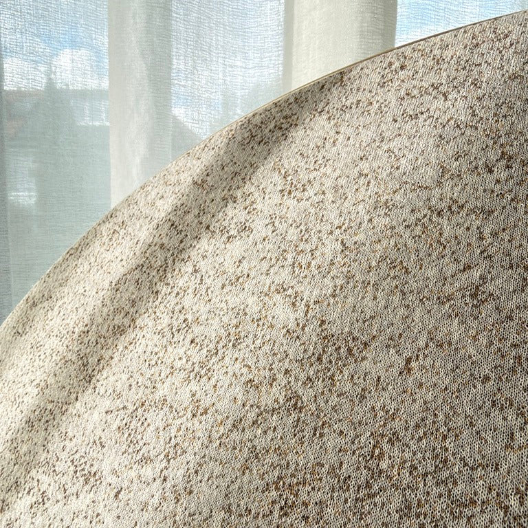 Bang & Olufsen Beoplay A9 and Beosound A9 Kvadrat Woolscape cover Golden by Bang & Olufsen, close-up of the cream and gold-flecked knitted wool cover crossed by a band of shadow, in front of sheer curtains in window light